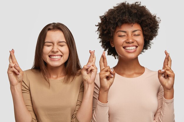 Le femmine soddisfatte di razza mista hanno sorrisi a trentadue denti, incrociano le dita per fortuna o fortuna