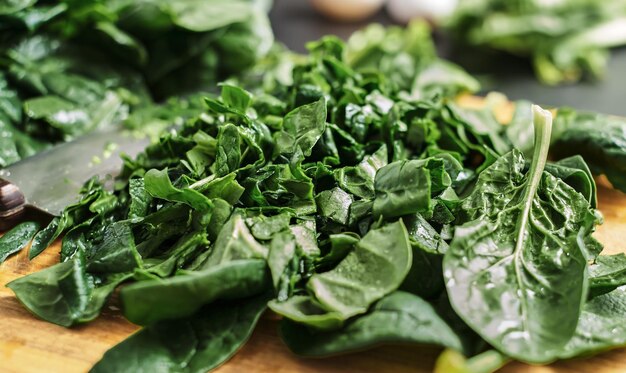 Le foglie di spinaci affettate verdi succose si trovano su un tagliere di legno. Messa a fuoco selettiva, primo piano di spinaci. L'idea di fare colazione con cibi sani e biologici