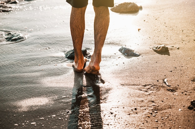 Le gambe dell&#39;uomo che camminano sulla sabbia puntellano vicino all&#39;acqua