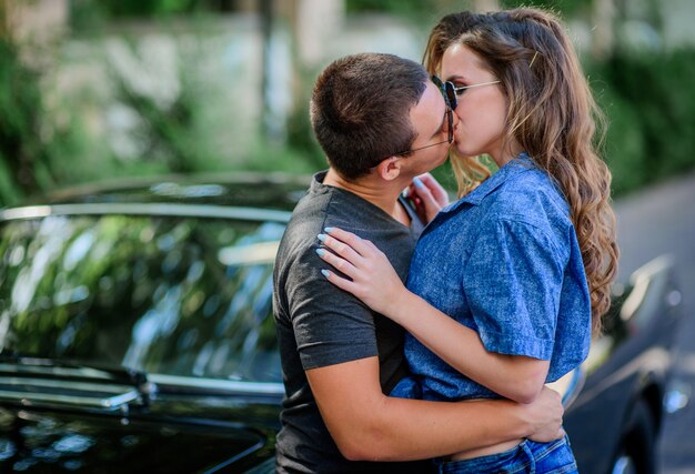 Le giovani coppie bacianti si sono vestite in uno stile casuale sta prima di vecchia automobile sportiva di retro