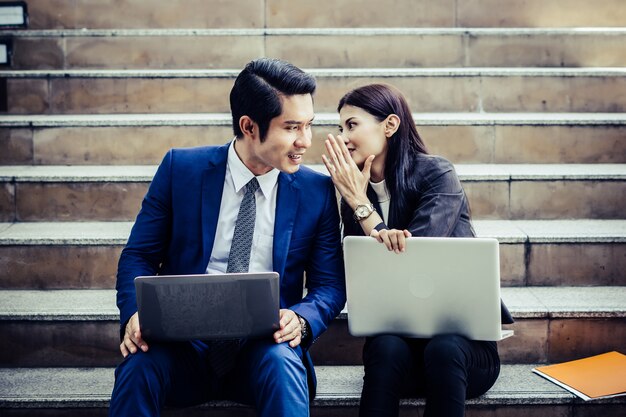 Le giovani coppie di affari che si siedono sulla scala che funziona alcuni prima vanno lavoro sul computer portatile.