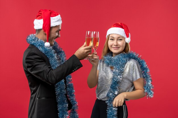 Le giovani coppie di vista frontale che celebrano il nuovo anno sui colori rossi della parete amano il Natale