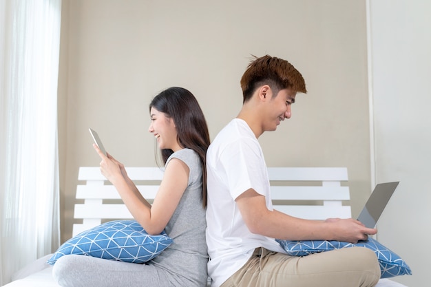 Le giovani coppie usano il dispositivo della tecnologia sul letto