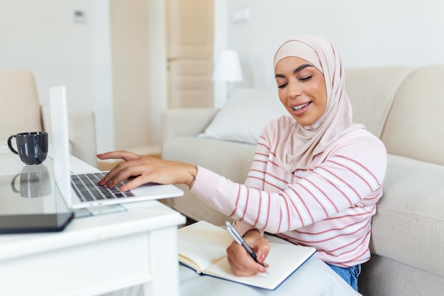Le giovani donne musulmane indossano l'hijab utilizzando la digitazione e il controllo dell'ordine dell'indirizzo del cliente sul computer portatile a casa mattina Concept business piccolo e negozio online