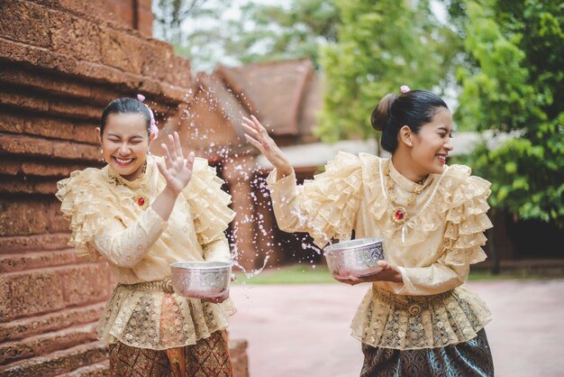 Le giovani donne sorridenti si vestono con splendidi costumi tailandesi spruzzando acqua nei templi e preservano la buona cultura del popolo tailandese durante il festival di Songkran, il giorno della famiglia di Capodanno tailandese ad aprile