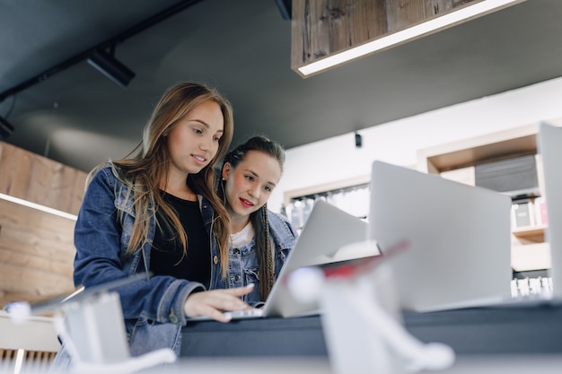 Le giovani ragazze attraenti in un negozio di elettronica utilizzano un computer portatile in una mostra. concetto di acquisto di gadget.