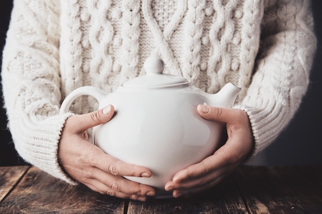 Le mani della donna adulta abbracciano la grande teiera in ceramica con una bevanda calda all'interno.