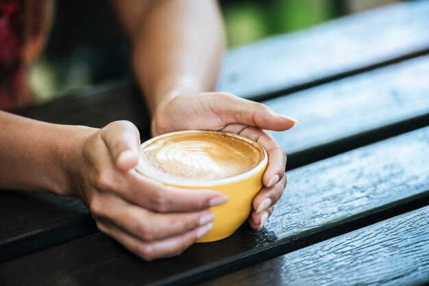 Le mani della donna che tengono tazza di caffè al caffè