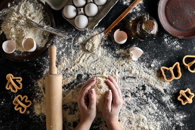 Le mani della donna impastano la pasta sul tavolo con farina, uova e ingredienti sul tavolo nero. Vista dall'alto. Natura morta. Disposizione piatta