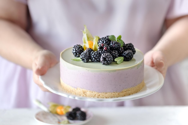 Le mani della ragazza tengono una cheesecake a base di frutti di bosco e tè matcha