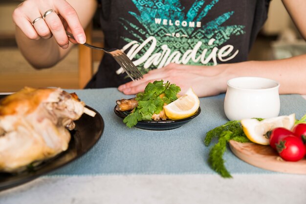 Le mani di una persona che usa la forchetta mentre mangiano pollo alla griglia a cena