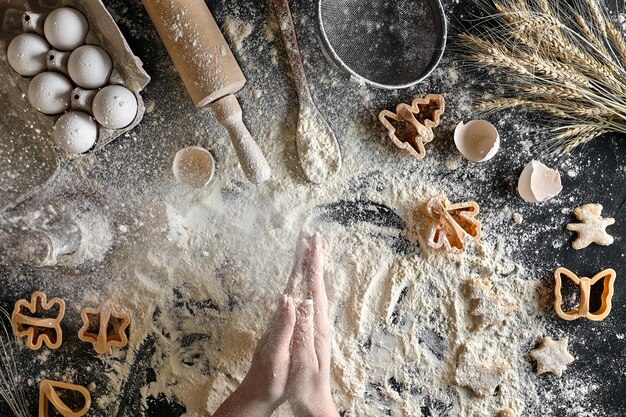 Le mani femminili di vista superiore preparano un posto per cucinare la pasta. Ingredienti per l'impasto e gli stampini per biscotti. Natura morta. Disposizione piatta