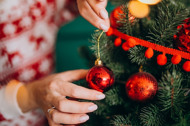 Le mani femminili si chiudono su, decorando l'albero di Natale con le palle rosse