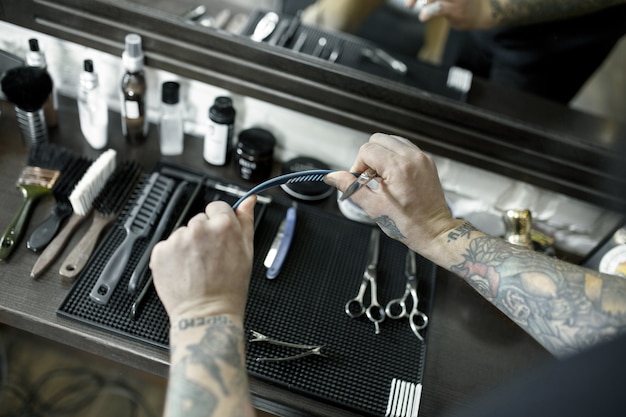 Le mani maschili e gli strumenti per tagliare la barba al negozio di barbiere.