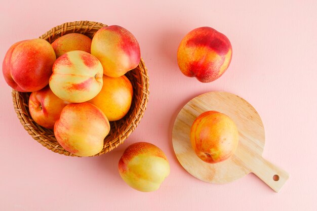 Le nettarine in un cesto piatto giacevano sul tavolo rosa e tagliere