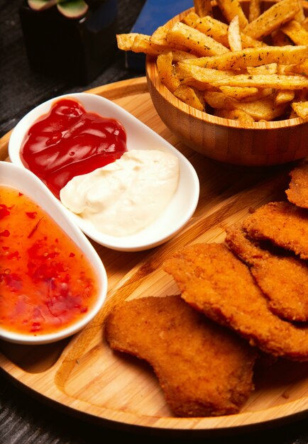 Le pepite di pollo sono servite con le patate fritte, il ketchup e la maionese sul bordo di legno