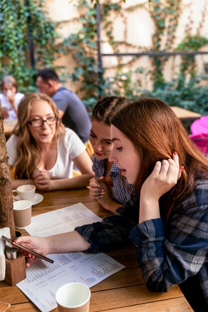 Le ragazze caucasiche stanno guardando la facciata di un telefono cellulare con i migliori amici al caffè alla moda