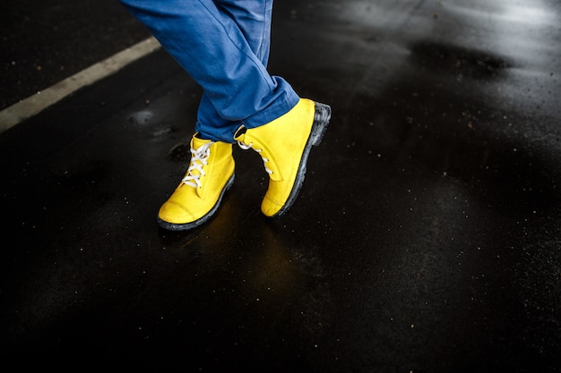 Le scarpe dell'uomo giallo sopra il fondo bagnato della via piovosa