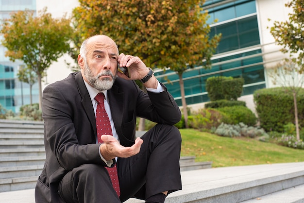 Leader di affari maturi confuso che parla sul cellulare