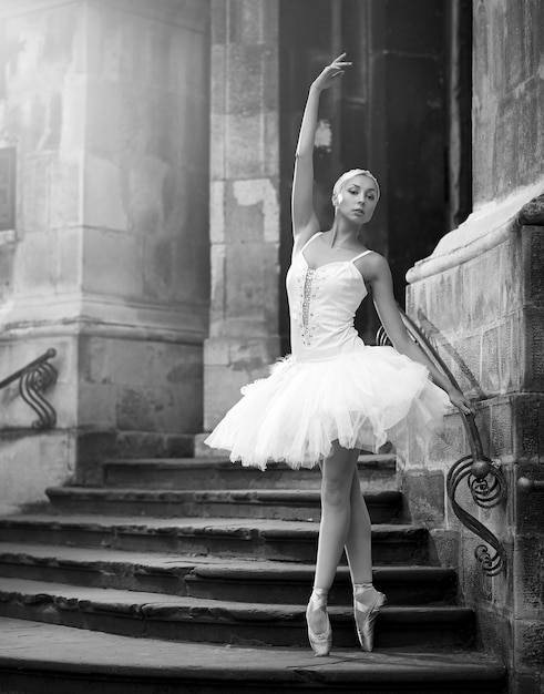 Lei è un'arte vivente. Scatto verticale monocromatico di una bellissima ballerina in piedi in posa di balletto sulle scale di un vecchio castello soft focus