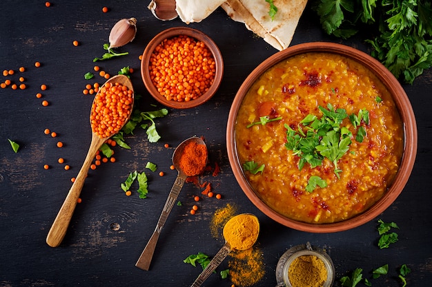 Lenticchie di zuppa indiana tradizionale. Curry piccante indiano Dhal in ciotola, spezie, erbe, tavola di legno nera rustica