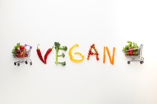 Lettering vegano fatto di verdure con piccoli carrelli della spesa