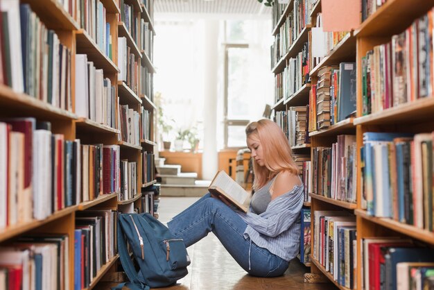 Lettura femminile dell&#39;adolescente sul pavimento delle biblioteche