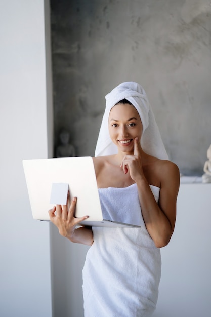 Libero professionista donna in asciugamano bianco stare in bagno con un computer portatile