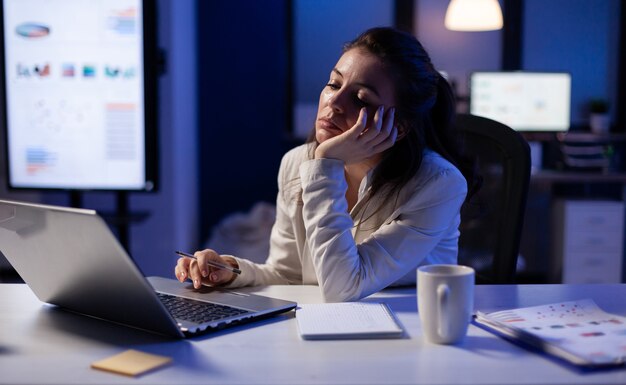 Libero professionista esausto che si addormenta davanti al laptop che controlla i rapporti finanziari nell'ufficio dell'azienda a tarda notte