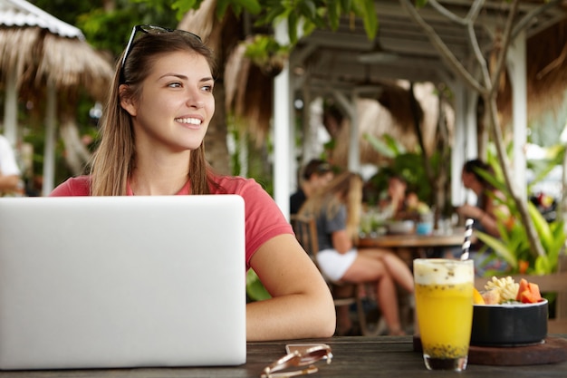 Libero professionista femmina caucasica con acconciatura lunga che lavora in remoto sul moderno pc portatile, utilizzando il wi-fi gratuito durante la colazione al bar