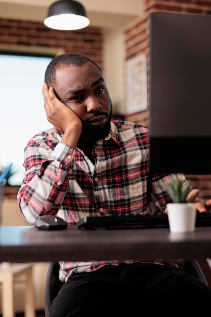 Libero professionista stanco e sfinito che lavora da remoto, si sente stressato e oberato di lavoro per il lavoro online. Essere infelici e frustrati alla scrivania, fare un lavoro a distanza sul computer. Operaio assonnato.