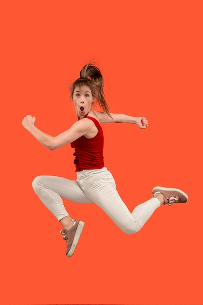 Libertà di movimento. Colpo a mezz'aria di giovane donna abbastanza felice che salta e che gesturing contro il fondo arancio dello studio.