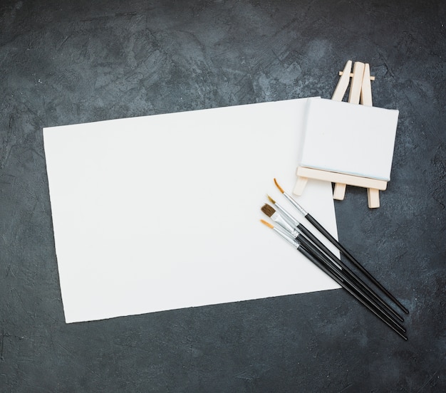 Libro bianco in bianco con mini cavalletto e pennello su sfondo di ardesia