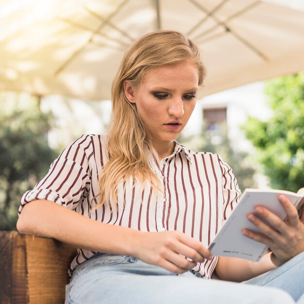 Libro di lettura attraente della giovane donna a all&#39;aperto