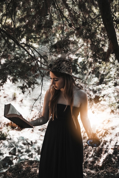 Libro di lettura della giovane donna con la candela a disposizione in foresta