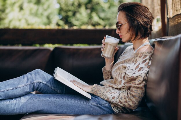 Libro di lettura della giovane donna e caffè bevente