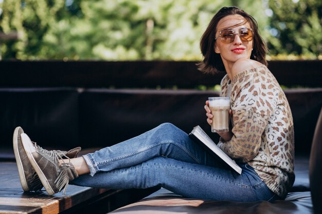 Libro di lettura della giovane donna e caffè bevente