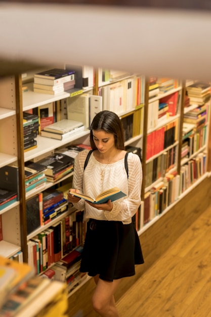 Libro di lettura della giovane signora vicino allo scaffale