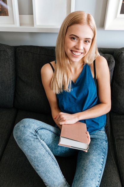 Libro di lettura e di seduta della giovane donna graziosa allegra a casa