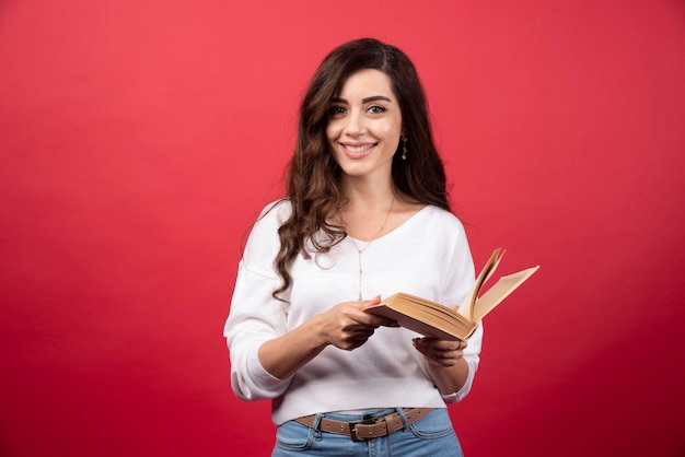 Libro lettura donna in piedi su uno sfondo rosso. Foto di alta qualità