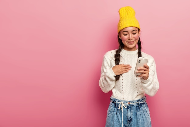 Lieta bruna donna coreana utilizzando il telefono cellulare su sfondo rosa