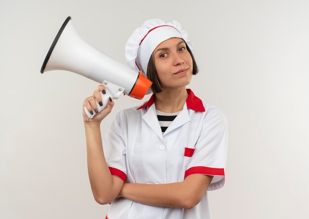 Lieta giovane cuoca in uniforme da chef tenendo l'altoparlante isolato sulla parete bianca