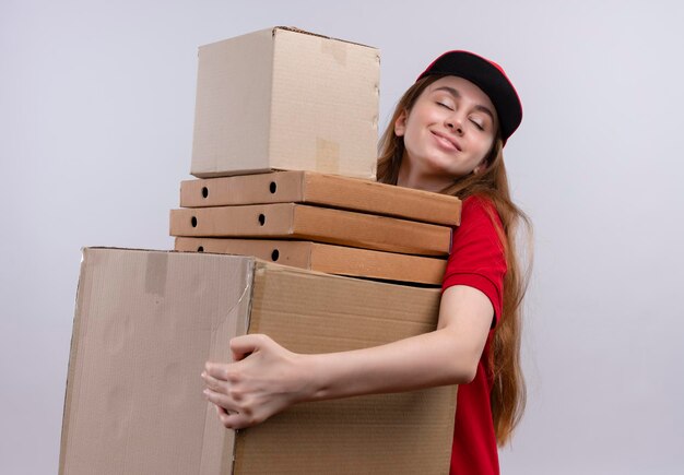 Lieta giovane ragazza di consegna in rosso uniforme che tiene scatole e pacchetti su uno spazio bianco isolato