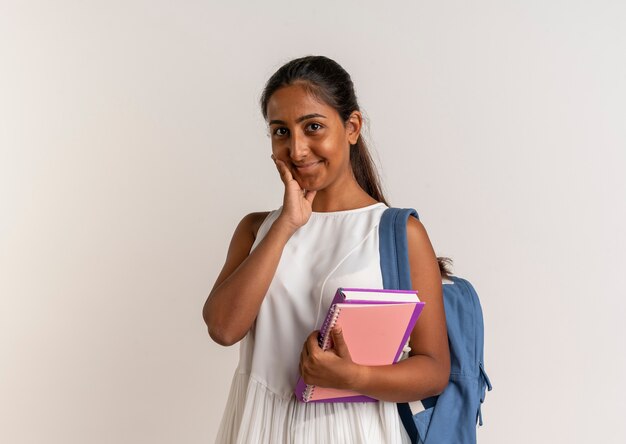 Lieta giovane studentessa indossa il taccuino della tenuta della borsa posteriore e mette la mano sulla guancia su bianco