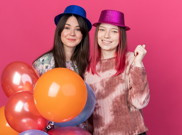 Lieto di guardare la telecamera ragazze che indossano un cappello da festa con in mano palloncini