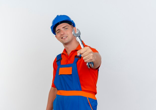 Lieto giovane costruttore maschio che indossa l'uniforme e il casco di sicurezza tenendo fuori la chiave per la fotocamera su bianco