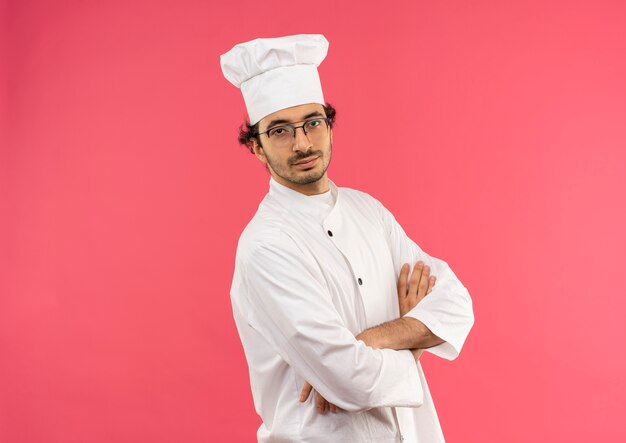 lieto giovane cuoco maschio che indossa l'uniforme dello chef e bicchieri attraversando le mani