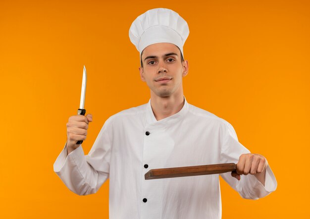 Lieto giovane maschio cool chef indossa uniforme tenendo coltello e tagliere