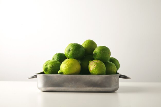 Limette fresche in una casseruola d'acciaio sul tavolo bianco.