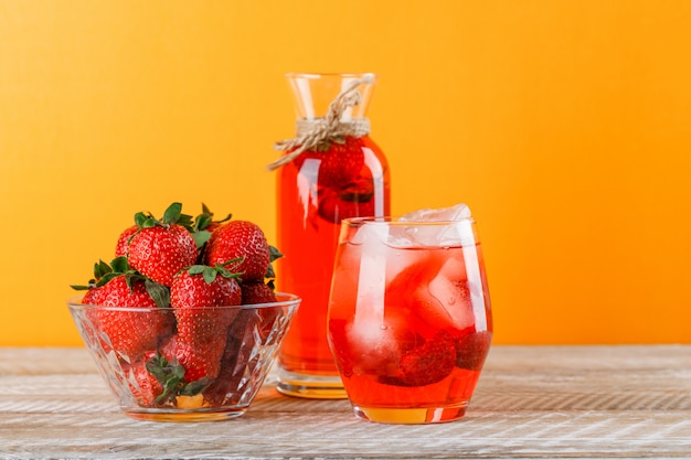 Limonata con le fragole in brocca e vetro su fondo di legno e giallo, vista laterale.